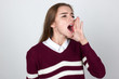 © kristiana1992 - Portrait of a pretty woman  in short sweater, white shirt screaming toward put two hands to her face  standing over gray background