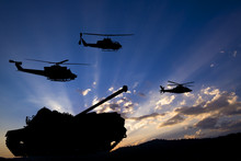Military Tank And Helicopters Silhouetted Against Dawn Or Dusk Blue Sky