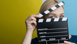 © Myvisuals - Young woman holding a clapperboard over colorful backgound