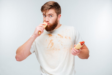 Hungry bearded man in dirty shirt biting hotdog