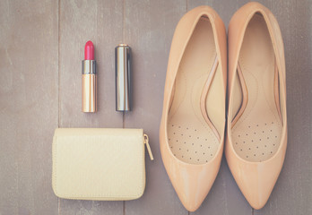 Nude colored high heels still life with wallet and red lipstick, top view, retro toned