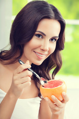 Wall Mural - Smiling young woman eating grapefruit at home