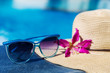 Sunglasses with flower and straw hat on border swimming pool