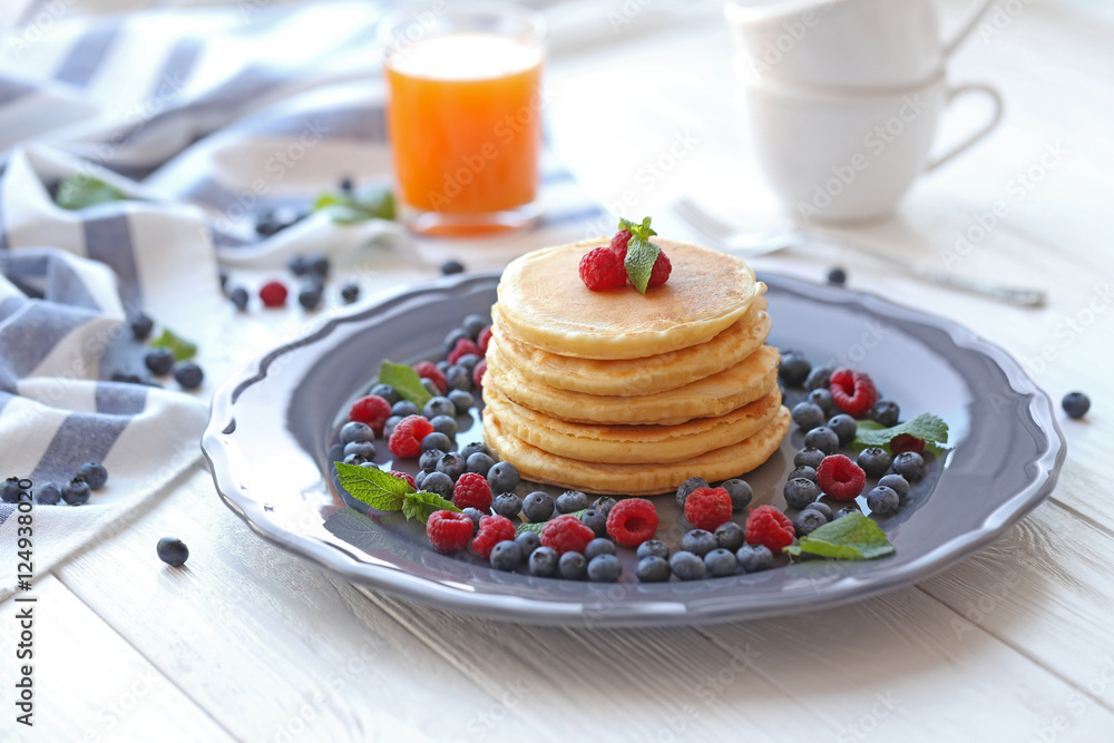 Plate with tasty pancakes and berries on wooden table
