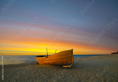 Photographie Un bateau de pêche orange sur la plage au coucher du soleil