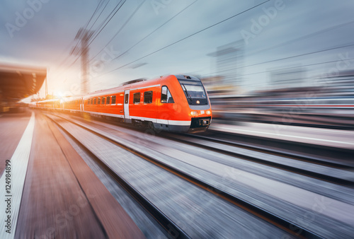 Cuadros en Lienzo Hermosa estación de ferrocarril con el tren de cercanías rojo de alta velocidad moderna con efecto de desenfoque de movimiento en la puesta de sol de colores