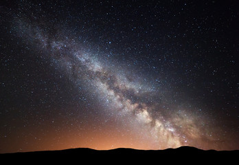 Night landscape with amazing Milky Way and yellow light at mountains. Starry sky with hills at summer. Beautiful Galaxy.l Universe. Space background