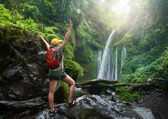 Wall Mural - young woman backpacker enjoying view at waterfall in jungles.