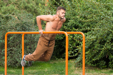 young man doing triceps dip on parallel bars outdoors