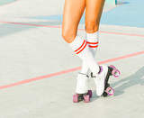 Beautiful long-legged girl posing on a vintage roller skates in denim shorts and white T-shirt in the skate park on a warm summer evening. Part of body.