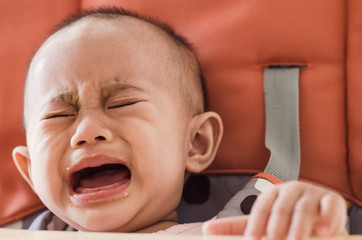 Asian baby girl sitting in highchair and crying refuses to eat f