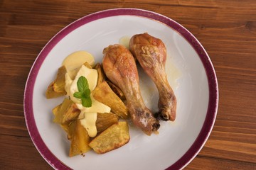 Roasted chicken drumsticks served on the old vintage porcelain plate with baked sweet potatoes and french mustard sauce. Picture isolated on the wooden table closeup. Fresh and healt family lunch.