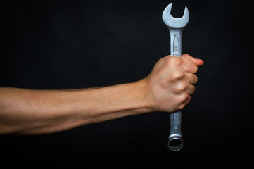 Man's hand holding a wrench. On a black background.