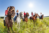 Fototapeta  - Happy equestrians riding horses in summer meadow