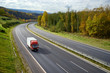 Asphalt road with a moving red small truck in the autumn landscape.