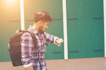 Young man looking at his hand-watch before go to travel with bac