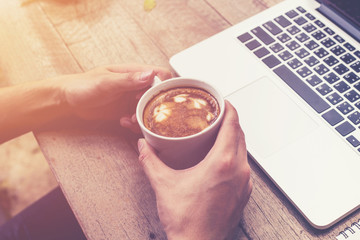 young business man hand holding cup coffee and using laptop comp