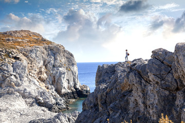 Wall Mural - Young woman tourist is standing on a high cliff overlooking the