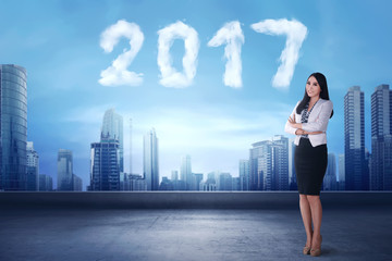 Smiling asian business woman standing beside cloud shaped number 2017
