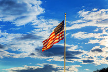 American Flag Flying In The Breeze Against A Blue Sky With White Clouds