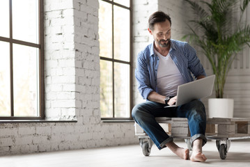 Positive delighted man holding a laptop on his knees