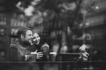 Canvas Print - Happy and romantic caucasian couple in warm sweaters drink coffee from disposable paper cups in cafeteria. Holidays, christmas, winter, love, hot drinks, people concept