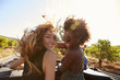 © Monkey Business - Two women standing in the back of open car turning to camera