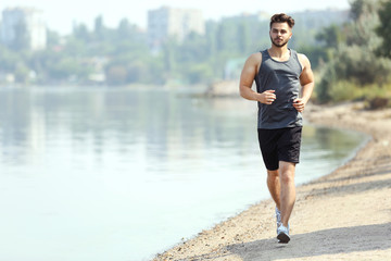 Wall Mural - Handsome man jogging on river bank