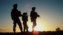 Squad Of Three Fully Equipped And Armed Soldiers Standing In Desert Environment In Sunset Light. Slow Motion.