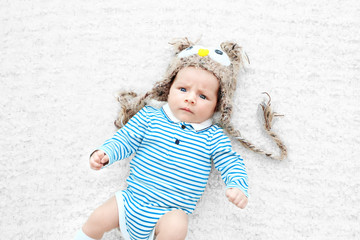 Poster - Cute baby with funny knitted cap lying on white bedspread, close up view