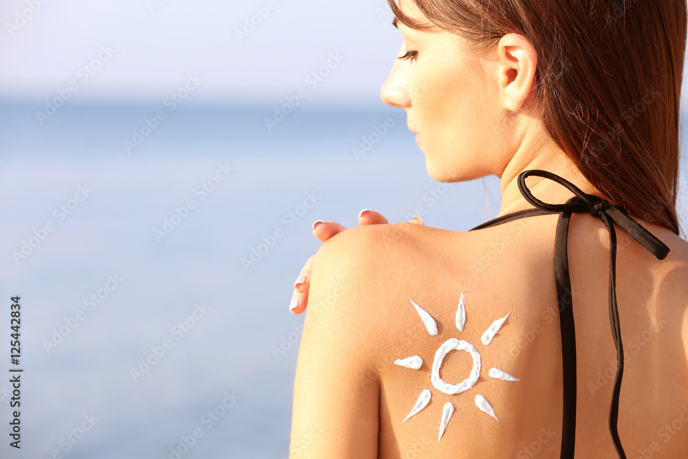 Young woman with sunscreen on back,  sea background