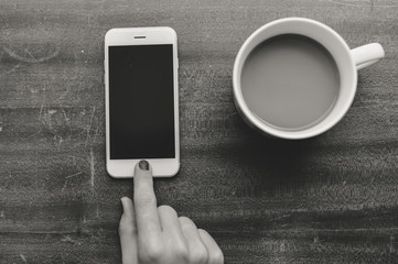 Top view on hand using smartphone and holding cup of coffee, wooden table background