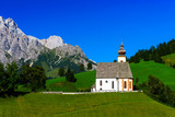 Fototapeta Londyn - Beautiful little church in Alps. Sunny day, green grass on the h