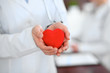 © rogerphoto - Female doctor with stethoscope holding heart.  Patients couple sitting in the background