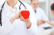 © rogerphoto - Female doctor with stethoscope holding heart.  Doctor and patient sitting in the background