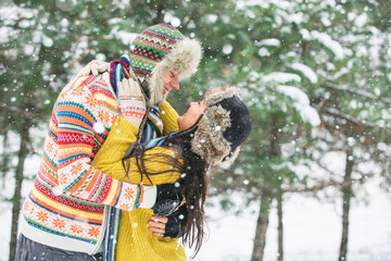 Couple in love walking in the winter woods. Pine Forest, spruce trees. Happy man and a woman. People dressed in sweaters and hats. Emotional people. Snowfall.