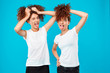Two girls twins holding hair, joking over blue background.