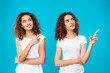 Two girls twins smiling, pointing fingers away over blue background.