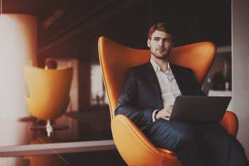 young serious successful man entrepreneur in formal business suite with a beard sitting on orange ar