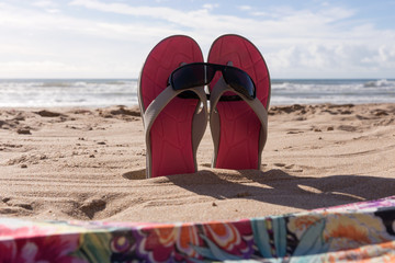 Wall Mural - Pair flip flops with sunglasses in the sand of beach, Travel background