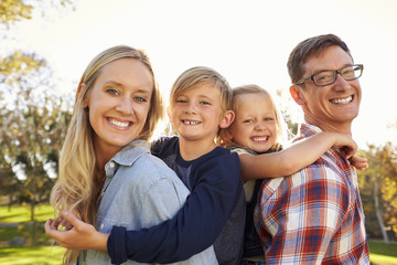 Parents carry their two young kids piggyback in a park, close up