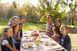 © Monkey Business - Two families having a picnic at a table look to camera