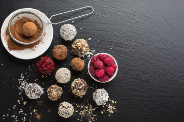 Wall Mural - Homemade chocolate candy ballsHomemade chocolate and nuts candy balls with cocoa powder, coconut, berries and chopped hazelnuts on black stone background, top view. Healthy Eating concept