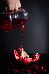 Wall Mural - Hand pours juice on pomegranate. On a black background.