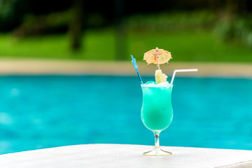 Glass of blue cocktail at swimming pool in summer time