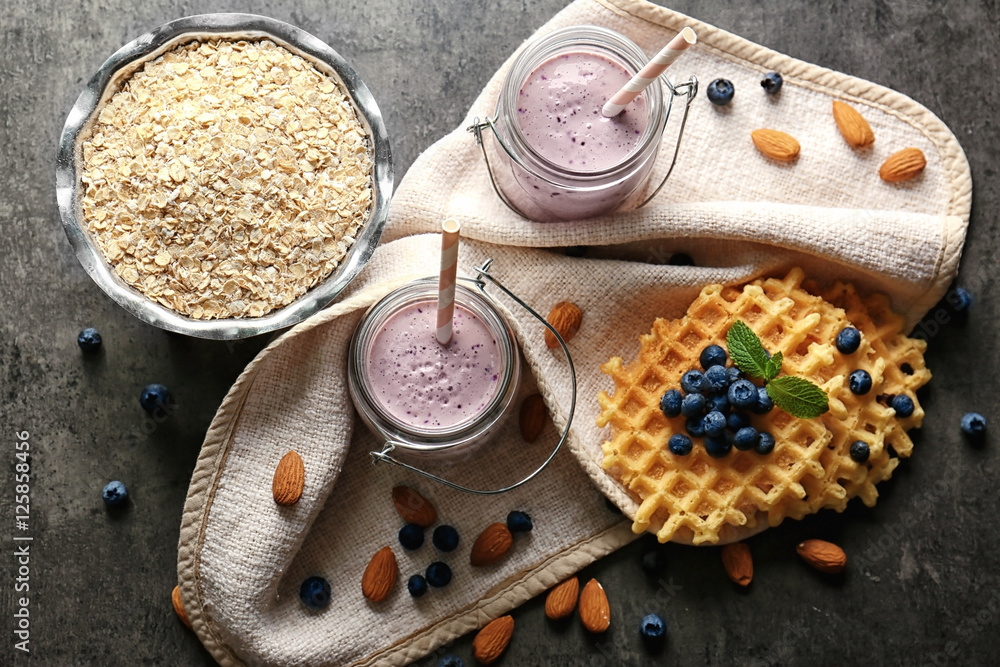 Two mason jars with tasty smoothie, wafers and some ingredients on grey table