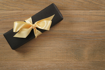 black rectangle gift box with champagne color ribbon bow on wooden oak table from above