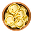 Tortelloni pasta in wooden bowl. Ring-shaped stuffed Italian dumplings with same shape as tortellini, but larger. Uncooked filled durum wheat semolina noodles. Macro food photo over white.