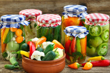Canned And Fresh Vegetables. Canned Tomatoes, Peppers And Pickled Cucumbers In Glass Jars On Wooden Table.