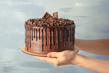 Female hands holding chocolate cake on light background